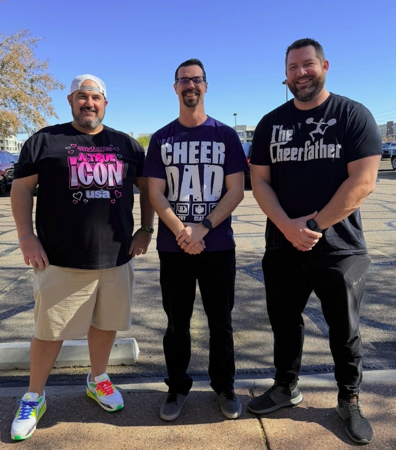 Tom, Geoff, and David — the hosts of Cheer Dads Unfiltered — laughing together at a competitive cheer arena.